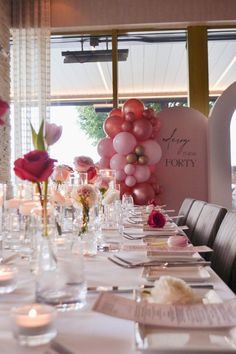 a long table set for a party with balloons and flowers on the wall behind it