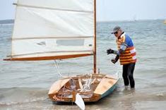 a man standing in the water next to a small sailboat on the ocean shore