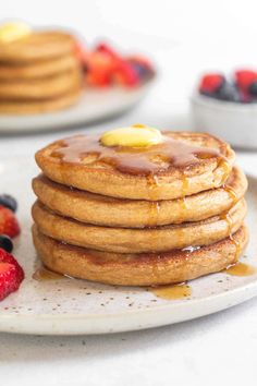 stack of pancakes with syrup and fruit on the side