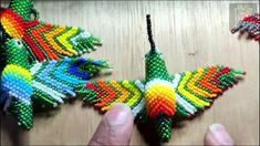 the beads are being made to look like colorful birds on a wooden table with one hand