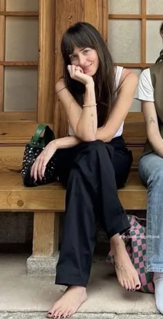 two people sitting on a bench with their feet propped up against the wall and one person holding her hand to her face