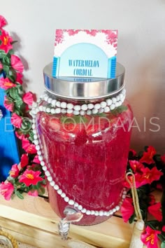 a jar filled with red liquid sitting on top of a table next to pink flowers