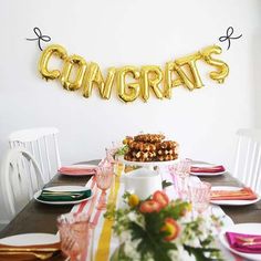 the table is set with plates, silverware and gold balloons that say congrats