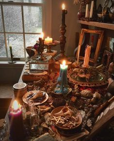 a table topped with lots of different types of items next to a window filled with candles