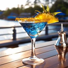 a blue martini with a pineapple garnish sits on a wooden table next to the water