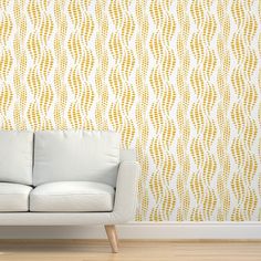 a white couch sitting in front of a wall with yellow and white designs on it