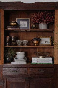 a wooden cabinet with dishes and vases on it's shelf next to a potted plant