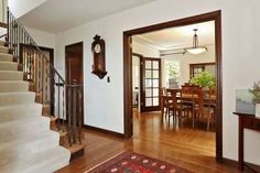 an entry way with stairs and a clock on the wall above it, leading to a dining room