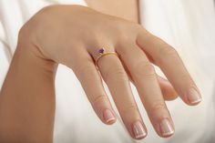 a woman's hand wearing a gold ring with an amethoraite stone