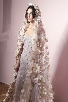 a woman in a white dress with flowers on it's head and veil over her face