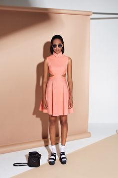 a woman standing in front of a wall wearing a pink dress and black shoes with her hands on her hips