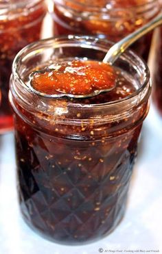 a spoon full of jam sitting on top of a white table next to other jars