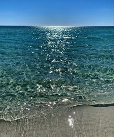 the ocean with clear blue water and sun reflecting off the sand at the beach in front of it