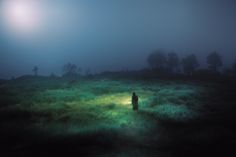 a person standing in the middle of a field at night with a light shining on them