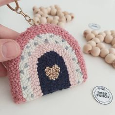 a hand holding a small crocheted keychain in front of some beads