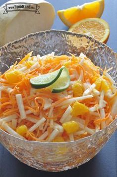 a glass bowl filled with shredded carrots and other vegetables next to sliced oranges