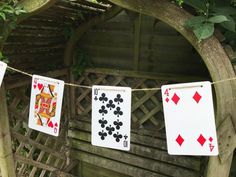 four playing cards are hanging on a clothes line in front of a wooden bench and trellis