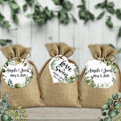 three bags filled with wedding favors sitting on top of a wooden table next to greenery