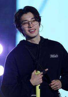 a young man with glasses and a black hoodie smiles at the camera while holding an umbrella