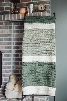 a green and white crocheted blanket sitting on top of a metal rack next to a brick wall