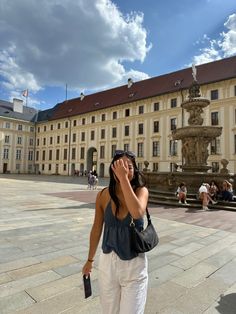 a woman is talking on her cell phone in front of a building with a fountain