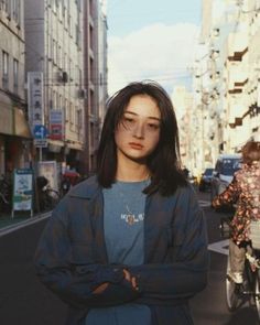 a woman standing in the middle of a city street with her arms crossed and looking at the camera