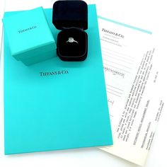 an open tiffany & co ring sits on top of a blue box next to some papers