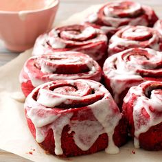 red velvet rolls with white icing sitting on top of a cutting board next to a pink bowl