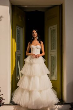 a woman standing in front of a doorway wearing a wedding dress with tiered layers