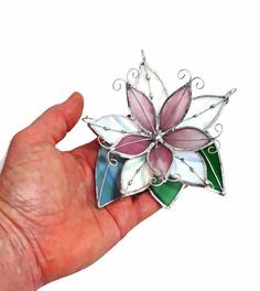 a hand holding a flower shaped brooch in it's left side, with green and pink petals