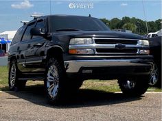 a large black truck parked on top of a parking lot next to other cars and tents