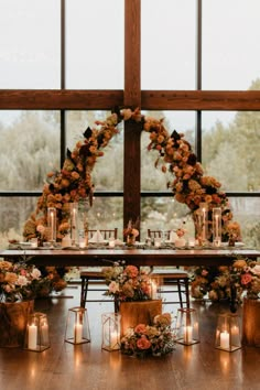 a table set up with candles and flowers on it for an outdoor wedding reception in front of a large window