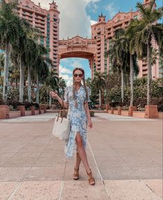 a woman standing in front of a large building with palm trees on both sides and an archway