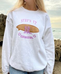 Introducing our "Surf's Up Cowgirl" Sweater - A perfect blend of coastal cowgirl charm and surfer girl style! This cozy sweater is designed for the adventurous spirit in you, combining the best of both worlds with a surfboard and cowgirl boots motif. Ride the waves in style with the iconic surfboard graphic, a nod to your love for the ocean while you also embrace your inner cowgirl. Crafted with quality and comfort in mind, this sweater will keep you warm on those breezy beach days and add a touch of whimsical flair to your outfit. Whether you're strolling along the shoreline or heading to a beach bonfire, this sweater is the ultimate expression of "Surf's Up, Cowgirl!" Don't miss out on this unique blend of coastal cowgirl and surfer girl style. Grab yours today and ride the waves in coas White Cotton Vsco Sweatshirt, White Relaxed Fit Top For Surfing, White Vsco Style Letter Print Sweatshirt, White Sporty Surfing Tops, Sporty White Surfing Tops, White Letter Print Sweatshirt For Beach Season, White Sporty Tops For Surfing, White Screen Print Sweatshirt For Summer, Sporty White Tops For Surfing