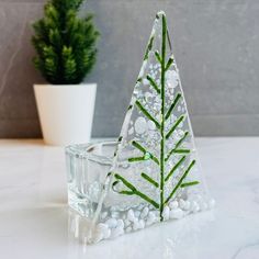 a small glass christmas tree sitting on top of a table next to a potted plant