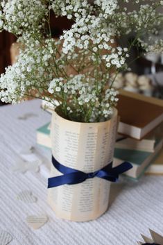 a vase filled with white flowers sitting on top of a table covered in books and paper