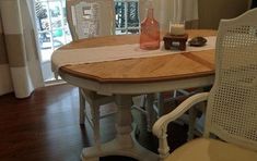 a dining room table with white chairs and a vase on top of it, in front of a sliding glass door