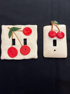 two white ceramic switch plates with cherries and leaves on them, one is painted red