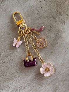 a key chain with charms attached to it on a stone surface next to a pink flower