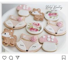 decorated cookies are arranged on a plate with pink flowers and leaves in the shape of animals