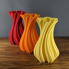 three different colored vases sitting on top of a wooden table next to each other