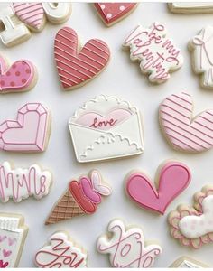 decorated cookies are arranged on a white surface with pink and red accents, including hearts, ice cream cones, and love letters