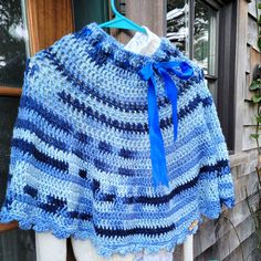 a blue and white crocheted shawl hanging on a window sill outside