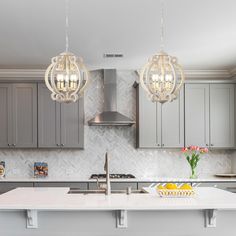 a kitchen with gray cabinets and white counter tops, two chandeliers hanging from the ceiling