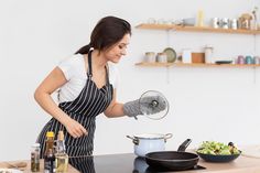 a woman in an apron is cooking on the stove top with a pot and pan