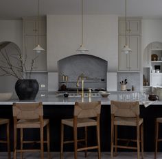 a kitchen with white cabinets and black countertops has chairs around the island, while gold accents are on the walls