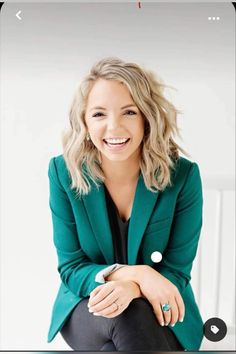 a woman sitting on top of a white chair wearing a green blazer and black pants