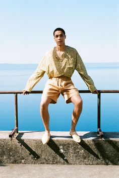 a man sitting on top of a metal rail next to the ocean with his legs crossed