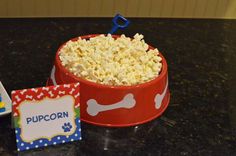 a red bowl filled with popcorn sitting on top of a table next to a card