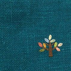 an embroidered tree on a teal blue fabric with multicolored leaves in the center